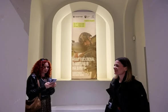 На фото: відвідувачки біля афіші фотовиставки "Хартія: Спека. 11 поглядів на війну" у підземеллі Ратуші у Львові, 4 квітня 2026 року